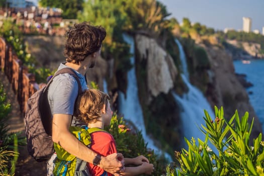 Father and son tourists on the background of Duden waterfall in Antalya. Famous places of Turkey. Lower Duden Falls drop off a rocky cliff falling from about 40 m into the Mediterranean Sea in amazing water clouds. Tourism and travel destination photo in Antalya, Turkey. Turkiye.