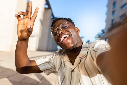 African american man with glasses taking selfie outdoors looking at camera waving hand. Lifestyle concept.
