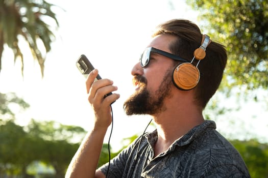 Side view of caucasian male recording voice message using mobile phone outdoors. Lifestyle concept.
