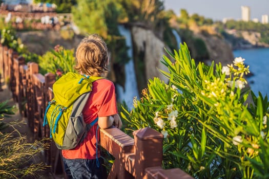 Boy tourist with a backpack on the background of Duden waterfall in Antalya. Famous places of Turkey. Lower Duden Falls drop off a rocky cliff falling from about 40 m into the Mediterranean Sea in amazing water clouds. Tourism and travel destination photo in Antalya, Turkey. Turkiye.