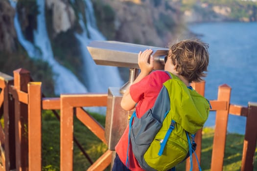 Boy tourist with a backpack on the background of Duden waterfall in Antalya. Famous places of Turkey. Lower Duden Falls drop off a rocky cliff falling from about 40 m into the Mediterranean Sea in amazing water clouds. Tourism and travel destination photo in Antalya, Turkey. Turkiye.