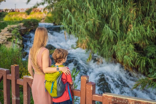 Mother and son tourists on the background of Duden waterfall in Antalya. Famous places of Turkey. Lower Duden Falls drop off a rocky cliff falling from about 40 m into the Mediterranean Sea in amazing water clouds. Tourism and travel destination photo in Antalya, Turkey. Turkiye.
