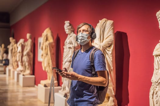 Portrait of contemporary man looking at sculptures and listening to audio guide at museum exhibition.