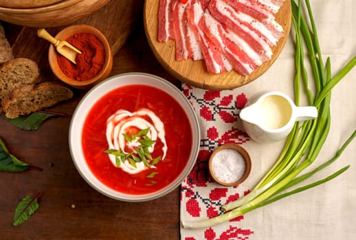 Traditional Ukrainian borsht, red vegetable soup or borscht with smetana on wooden background. Slavic dish with cabbage, beets, tomatoes Top view of a wooden tray on a black background on which lies Ukrainian food with spices Traditional Ukrainian towel along with garlic, bread and salt.