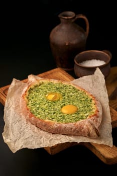 Traditional georgian pastry - adjarian khachapuri with cheese and raw yolk. Khachapuri with egg on wooden background in rustic style. Adjara khachapuri with ingredients.