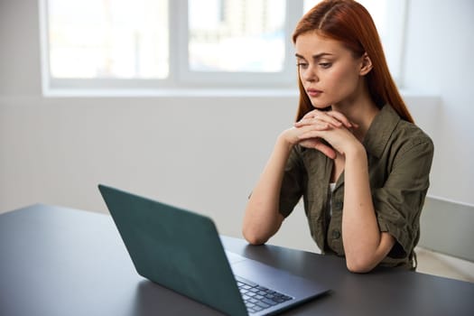 a serious, work-weary woman, with a sad face, sits at a laptop with her hands folded near her face. High quality photo