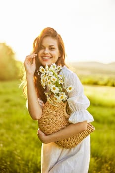 a laughing woman with a full basket of daisies stands in a light dress against the backdrop of a sunset in a field. High quality photo