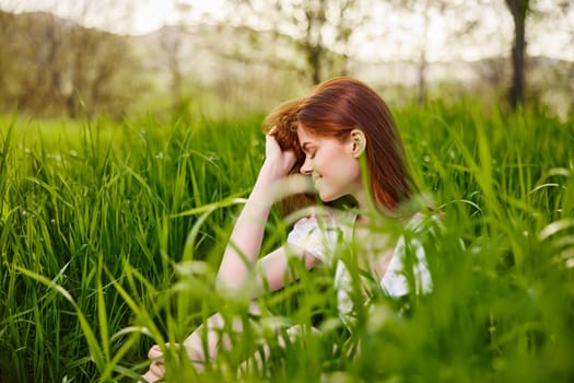 a young woman sitting resting in the tall grass straightening her hair. High quality photo