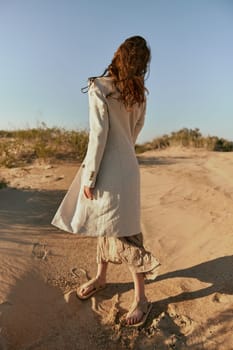 stylish woman in a light jacket posing on the sand, turning away from the camera. High quality photo