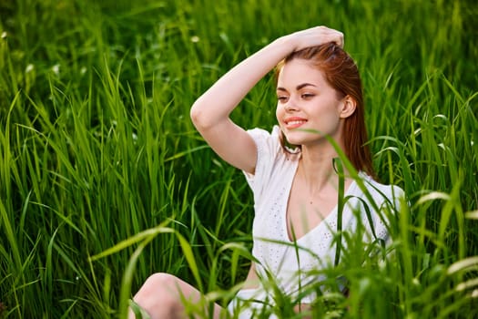cute woman with red hair sits in tall green grass with her hand on her head. High quality photo