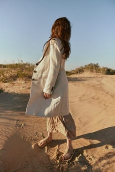 stylish woman in a light jacket posing on the sand, turning away from the camera. High quality photo