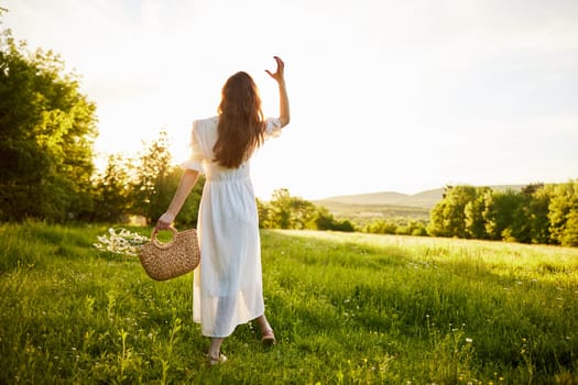 a girl in a long light dress stands in a field during sunset with her back to the camera. Full length photo. High quality photo