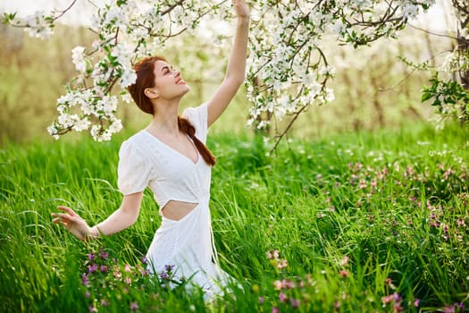 beautiful woman in a light dress posing next to a flowering tree in the countryside. High quality photo