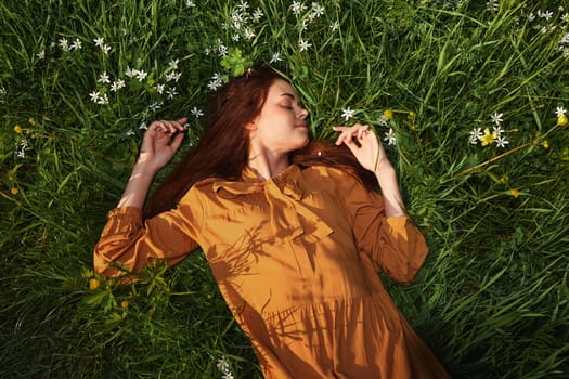 a relaxed woman, resting lying in the green grass, in a long orange dress, with her eyes closed and a pleasant smile on her face, recuperating, illuminated by the warm rays of the setting summer sun. High quality photo