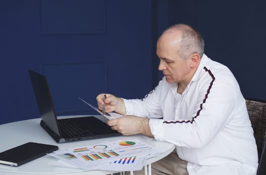 Male businessman works on laptops, studies reporting documents, charts and graphs.