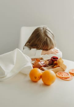 A girl in a white coat fell asleep or is sad sitting at a table on which stands a fruit marshmallow.