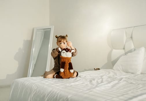 A girl in a dressing gown plays in bed with knitted toys.