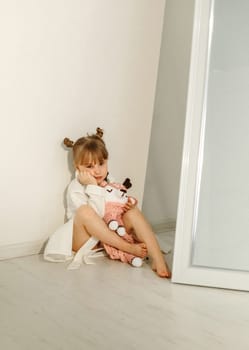A girl in a bathrobe plays on the floor with a knitted unicorn.
