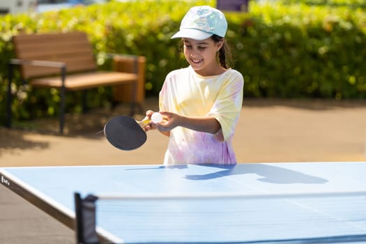 Young teenager girl playing ping pong. She holds a ball and a racket in her hands. Playing table tennis outdoors in the yard