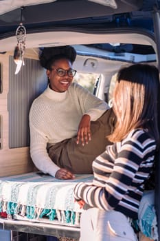 african woman laughing in a conversation with friend and enjoying van life, concept of weekend getaway with best friend and relaxation in camper van