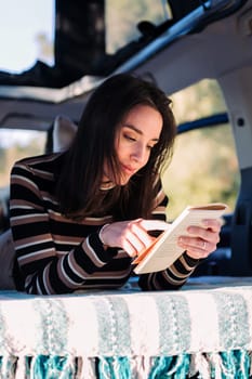 young caucasian woman relaxing in camper van reading a book, concept of road trip adventure and van life relaxation