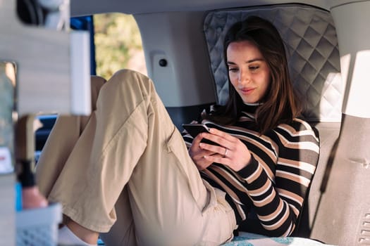 young caucasian woman relaxing in camper van using a mobile phone, concept of road trip adventure and van life relaxation