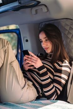 young caucasian woman relaxing in camper van using a mobile phone, concept of road trip adventure and van life relaxation