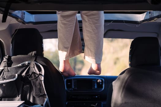 unrecognizable woman relaxing with feet dangling off the elevated bed of a camper van, concept of road trip adventure and van life relaxation