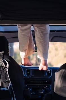 unrecognizable woman relaxing with feet dangling off the elevated bed of a camper van, concept of road trip adventure and van life relaxation