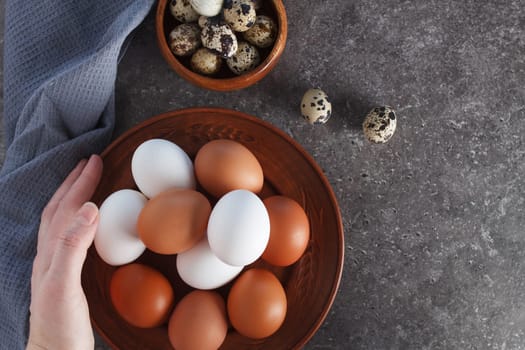 A woman's hand holds a chicken egg over a plate of eggs on the kitchen table.