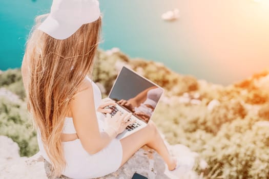 Digital nomad, Business woman working on laptop by the sea. Pretty lady typing on computer by the sea at sunset, makes a business transaction online from a distance. Freelance remote work on vacation