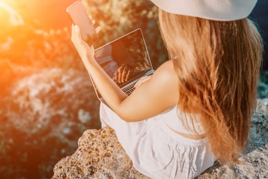 Successful business woman in yellow hat working on laptop by the sea. Pretty lady typing on computer at summer day outdoors. Freelance, travel and holidays concept.