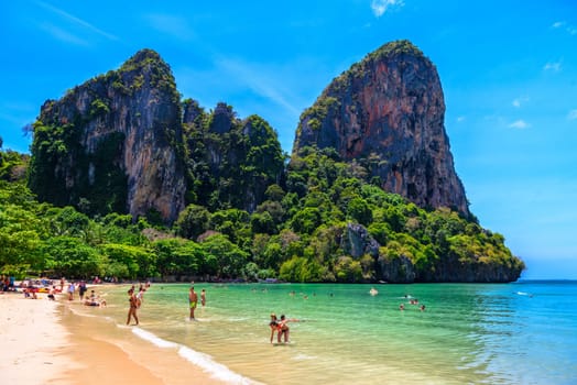 Rocks, water, tropical white sand beach and people swimming in emerald azure water of bay, Railay beach west, Ao Nang, Krabi, Thailand.