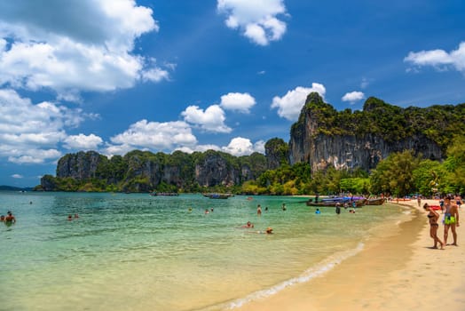 Rocks, water, tropical white sand beach and people swimming in emerald azure water of bay, Railay beach west, Ao Nang, Krabi, Thailand.
