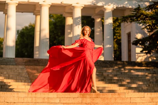 A woman in a long red dress against the backdrop of sunrise, bright golden light of the sun's rays. The concept of femininity, harmony