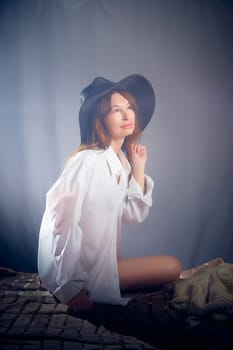 Portrait of a young sexy girl in white shirt and hat on a grey background. Classic style. dramatic portrait