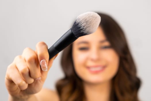 Young brunette model holding of big brush for applzing powder in front of face, selective focus