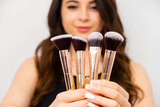 Attractive young woman holding golden makeup brushes. Professional makeup artist concept.