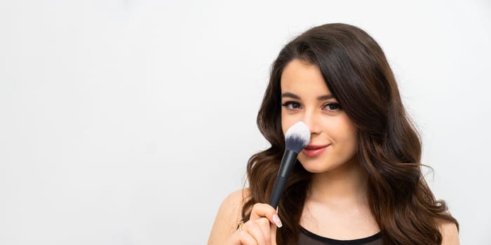Portrait of young attractive woman holding a cosmetic brush near her face, banner with copy space.