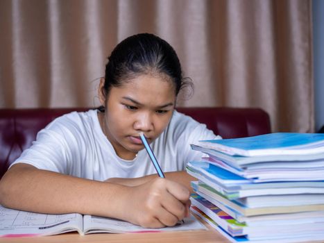 girl doing homework on a wooden table and there was a pile of books next to it The background is a red sofa and cream curtains.