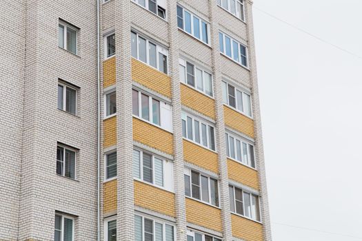 Facade of a high-rise building with plastic windows and balconies. Against the background of the gray sky. Modern new buildings, building facades. Real estate and urban architecture concept.