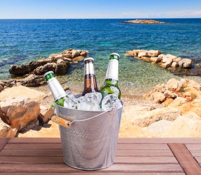 Three unopened bottles of beer inside ice bucket on beach background