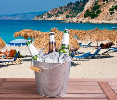 Three unopened bottles of beer inside ice bucket on beach background