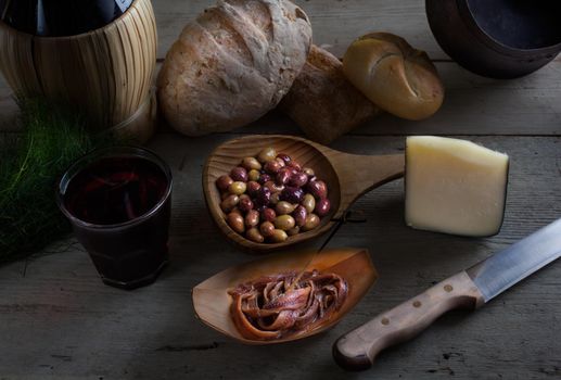 Italian slow food on the white table. Olives, cheese, bread, anchovies and red wine