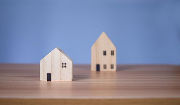 Two wooden model houses placed on a wooden table. with a light blue background