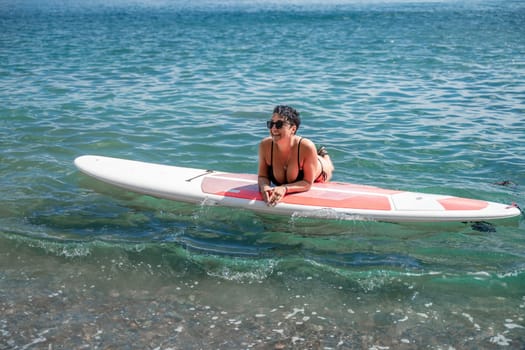 Woman sap sea. Sports girl on a surfboard in the sea on a sunny summer day. In a black bathing suit, he lies on a sap in the sea. Rest on the sea