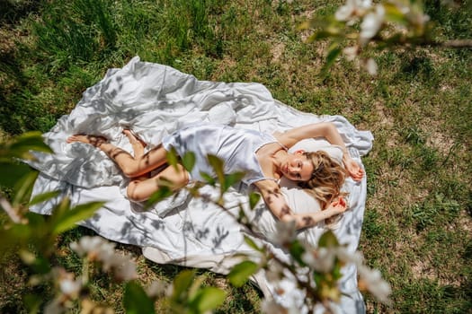 woman sleeps on a white bed in the fresh spring grass in the garden. Dressed in a blue nightgown