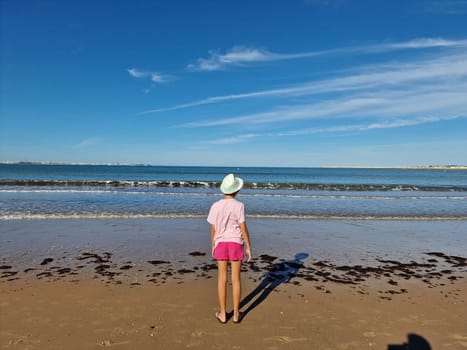 Girl with hat in front of the sea, on a sandy beach. Valdelagrana Beach in Puerto de Santa Maria, Cadiz, Andalusia, Spain