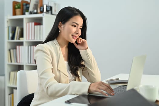 Charming asian woman working on online marketing, using laptop computer at workplace.