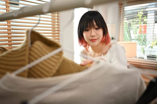 Young female fashion designer standing near clothing rack, working on new womenswear collection in modern studio.